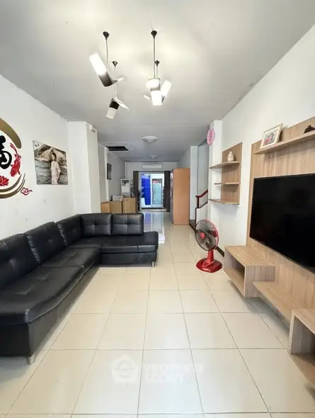 Spacious living room with modern black leather sectional and sleek wooden entertainment unit.