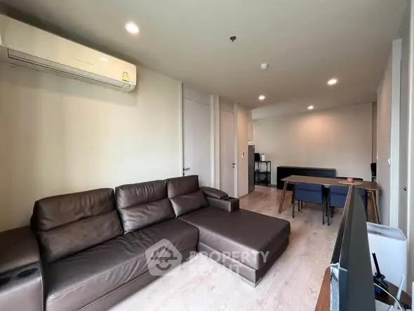 Modern living room with brown leather sofa and dining area, featuring sleek design and ample lighting.