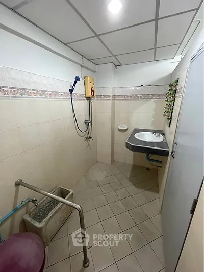 Compact bathroom with tiled walls and floor, featuring a wall-mounted sink and shower area.