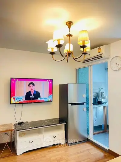 Modern living room with TV, fridge, and elegant chandelier lighting.