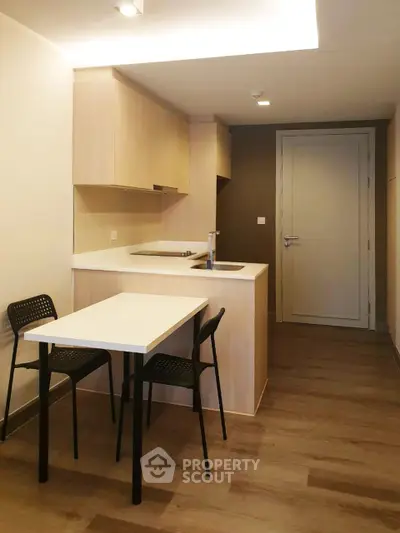 Modern compact kitchen with sleek wooden cabinetry and dining area in a cozy apartment.