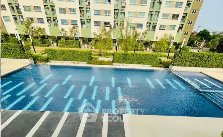 Modern apartment complex with a large swimming pool and lush greenery.