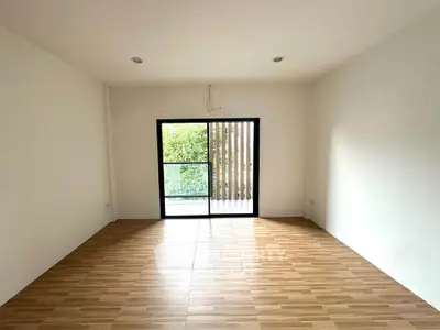 Spacious empty room with wooden flooring and large window leading to balcony.