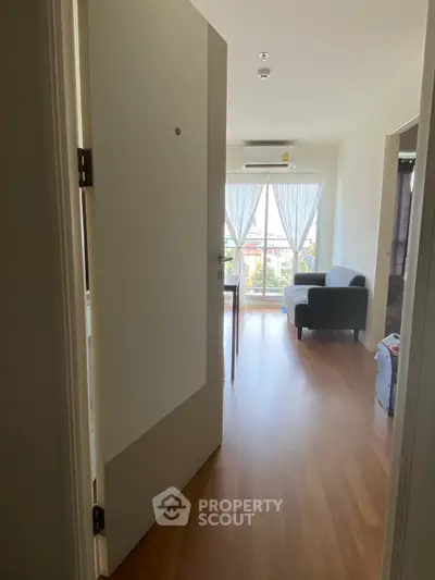Bright living room with wooden flooring and large window offering natural light and a cozy seating area.