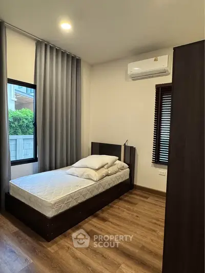 Cozy bedroom with wooden flooring and modern air conditioning unit, perfect for a comfortable living experience.