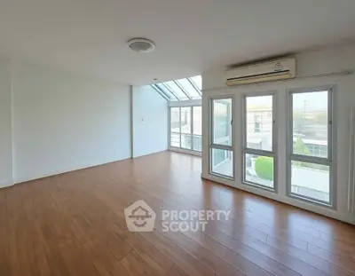 Spacious sunlit living room with wooden flooring and large windows in modern home.