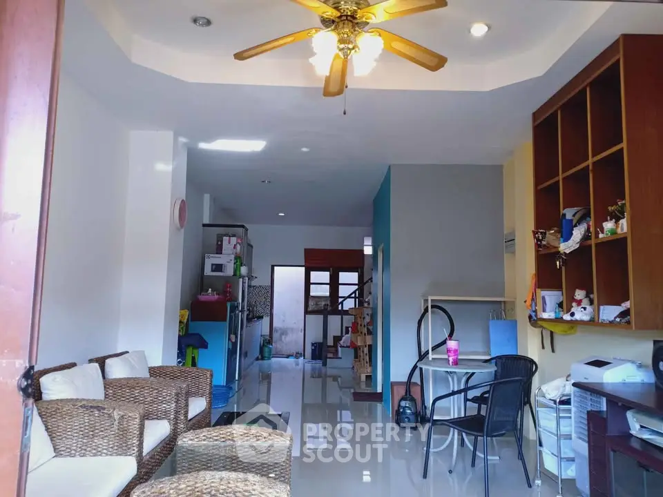 Spacious living room with wicker furniture and ceiling fan, open layout to kitchen area.