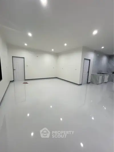 Spacious modern living room with sleek white flooring and recessed lighting, adjacent to a minimalist kitchen.