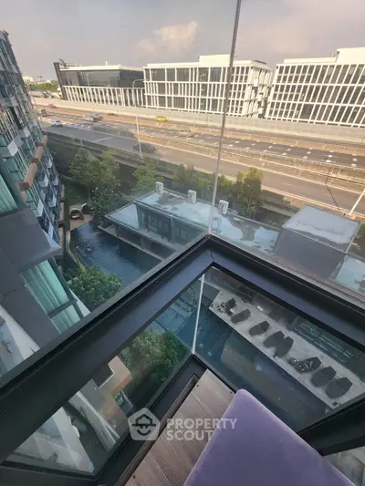 Stunning view from a modern high-rise balcony overlooking a pool and cityscape, perfect for urban living.