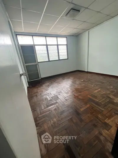Spacious empty room with wooden parquet flooring and large windows, ideal for customization.