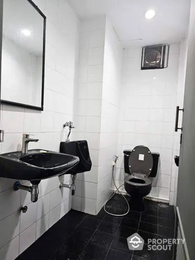 Pristine white-tiled bathroom featuring a sleek black sink, modern toilet, and large mirror, ideal for contemporary urban living.