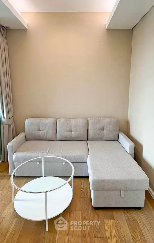 Modern living room with stylish gray sectional sofa and round white coffee table on wooden floor.