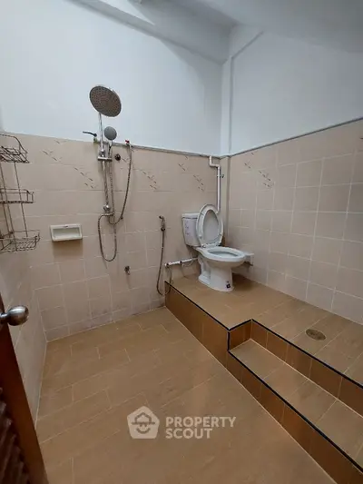 Spacious bathroom with modern fixtures, including a large shower area and a comfortable toilet, tiled for easy maintenance.