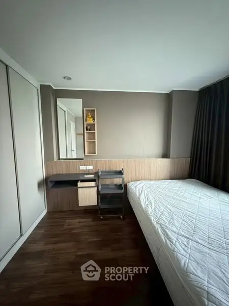 Modern bedroom with wooden flooring and built-in storage, featuring a sleek desk and large window.