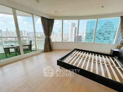 Spacious bedroom with panoramic city views and private balcony in luxury high-rise.