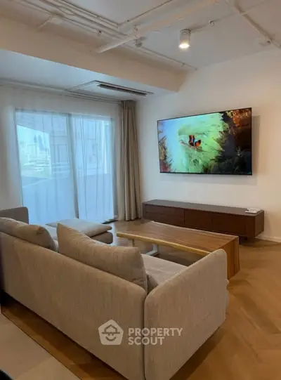Modern living room with large TV and stylish furniture, featuring a cozy ambiance and natural light.