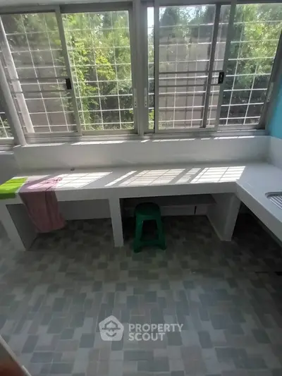 Bright kitchen area with large windows and tiled floor, featuring a green stool and colorful towels.