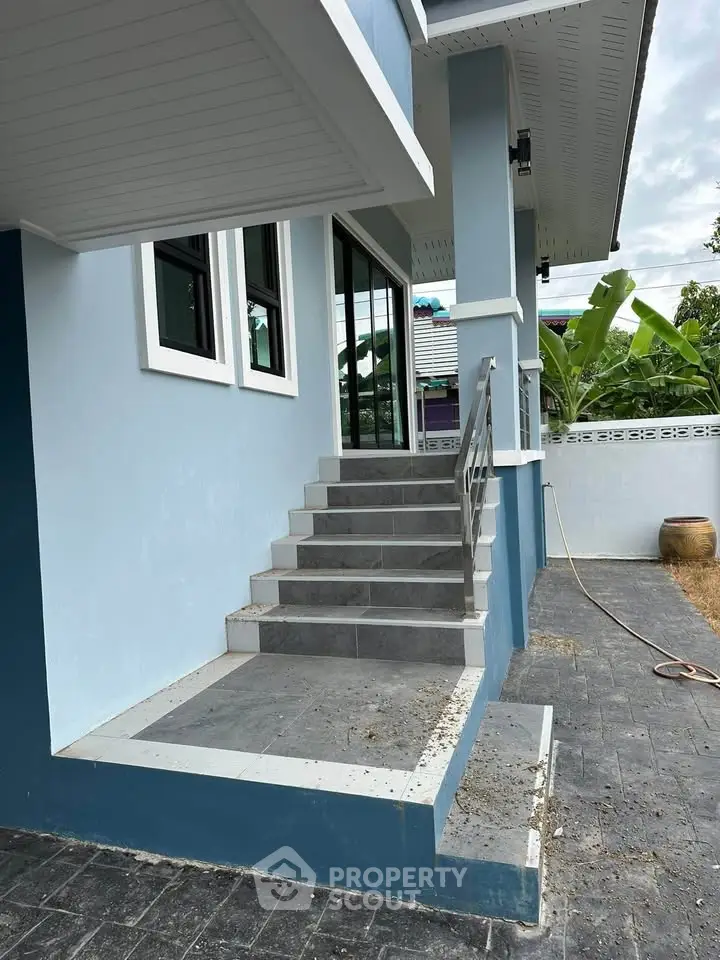 Charming blue exterior with modern staircase leading to a welcoming entrance, surrounded by lush greenery.