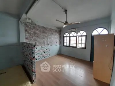 Spacious room with wooden flooring and unique brick accent wall, featuring large windows and ceiling fan.