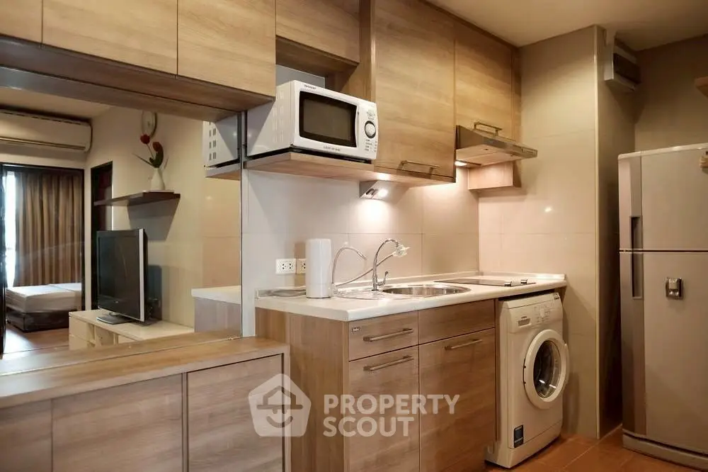 Modern kitchen with wooden cabinets, washing machine, and microwave in a cozy apartment.