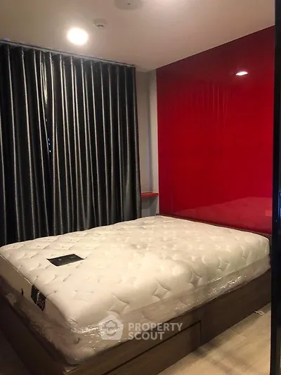 Modern bedroom with red accent wall and plush mattress in stylish apartment.