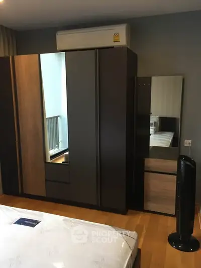 Modern bedroom with sleek wardrobe and air conditioning unit, featuring wooden flooring and stylish decor.