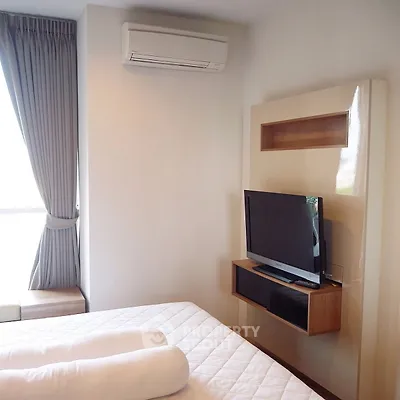Modern bedroom with wall-mounted TV and air conditioning, featuring elegant curtains and cozy bedding.