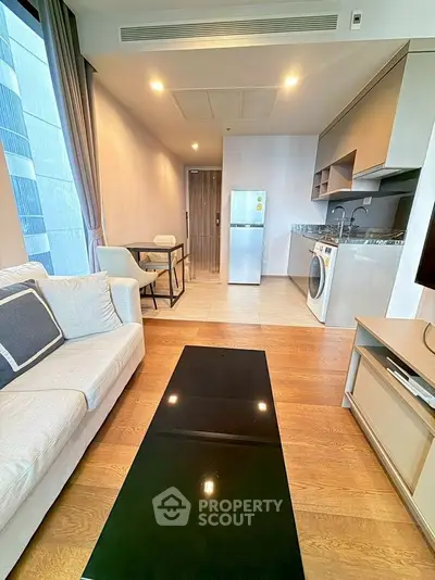 Modern living room with open kitchen, featuring a cozy sofa, dining area, fridge, and washing machine.