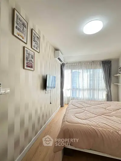 Cozy bedroom with modern decor and natural light, featuring a wall-mounted TV and stylish artwork.