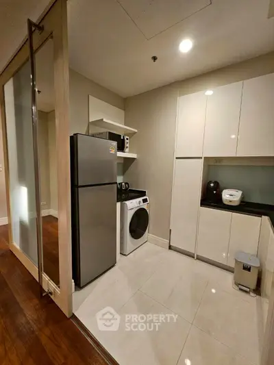 Modern kitchen with sleek appliances and ample storage space, featuring a washing machine and refrigerator.
