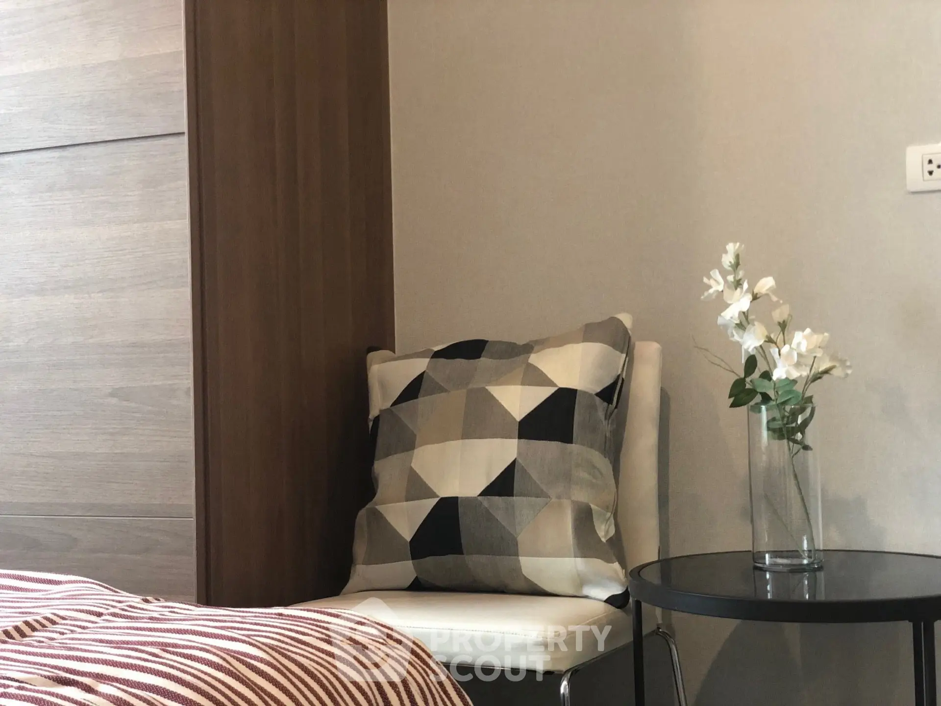Cozy bedroom corner with modern chair, geometric cushion, and elegant floral decor.