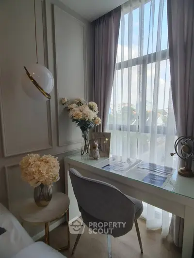 Elegant study nook with modern chair and floral decor by a sunlit window.