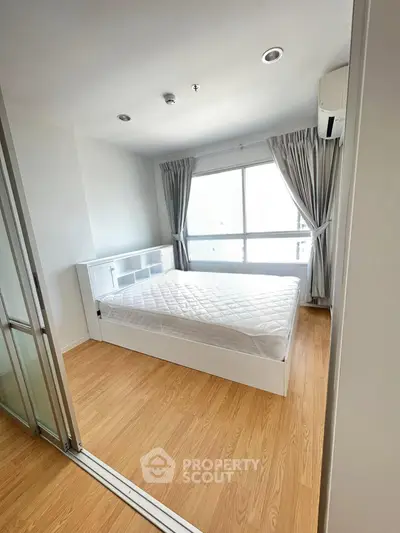 Bright and airy bedroom with wooden flooring and large window in modern apartment.
