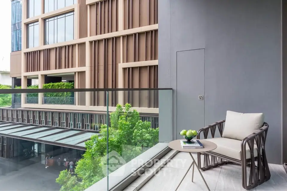 Stylish balcony with modern chair and table overlooking lush greenery and contemporary building facade.