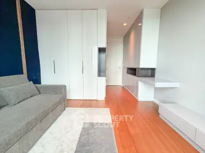 Modern living room with sleek white cabinetry and cozy gray sofa on wooden flooring.