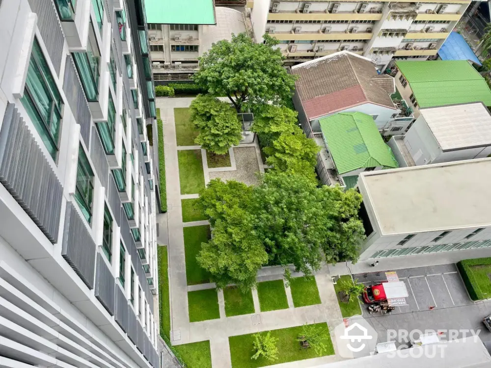 Stunning aerial view of modern apartment building with lush green courtyard and urban surroundings.