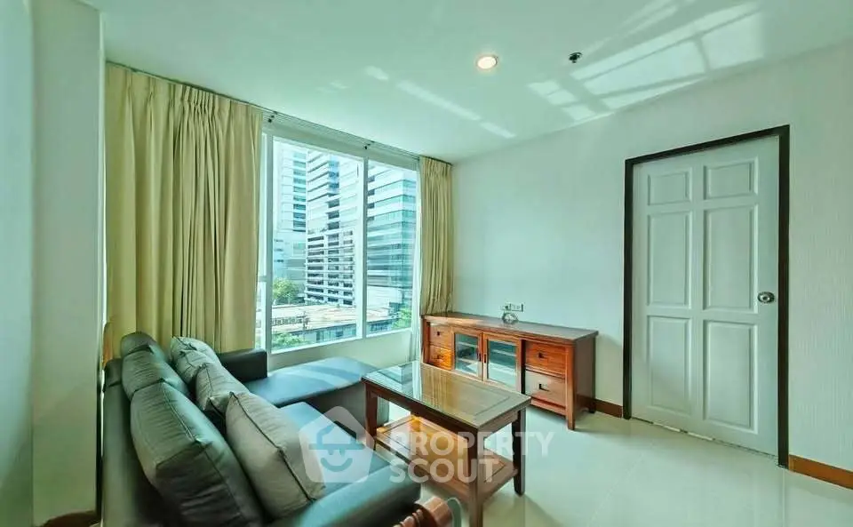 Bright living room with large window and city view, featuring modern furniture and natural light.