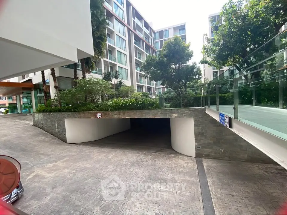 Modern residential building with lush greenery and underground parking entrance.