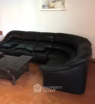 Spacious living room with elegant black leather sectional sofa and glass coffee table.