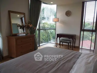 Elegant bedroom with large windows and stylish decor, offering a serene view of lush greenery.