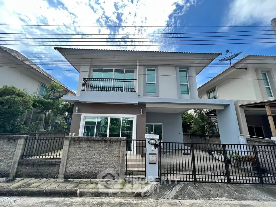 Modern two-story house with gated driveway and balcony in suburban neighborhood.