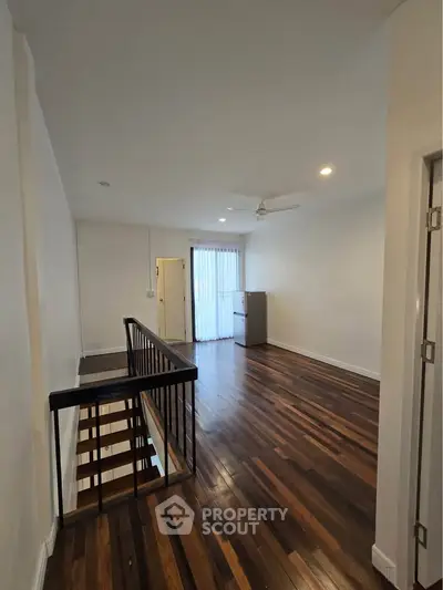 Spacious living area with wooden flooring and modern staircase in a bright apartment.