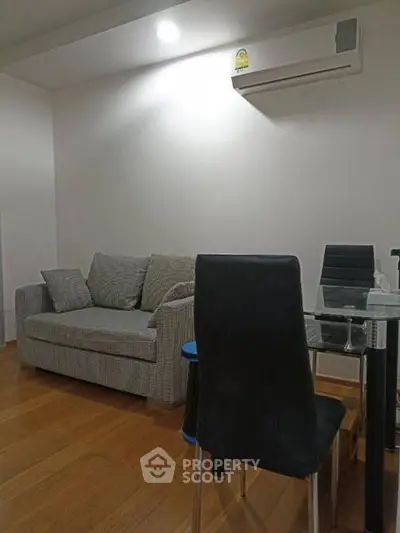 Cozy living room with modern sofa and dining area, featuring sleek wooden flooring and air conditioning.