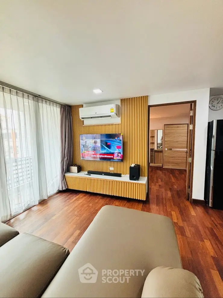 Modern living room with stylish wooden paneling and large TV, featuring sleek furniture and natural light.
