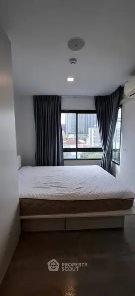 Spacious bedroom with large window offering city views, featuring a comfortable bed and modern decor.