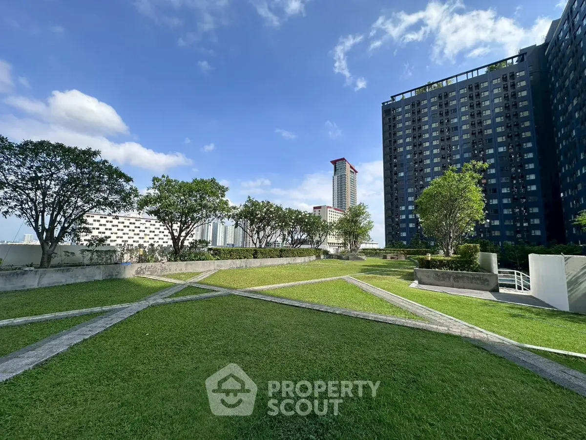 Spacious urban garden with lush greenery and modern high-rise buildings under a clear blue sky.