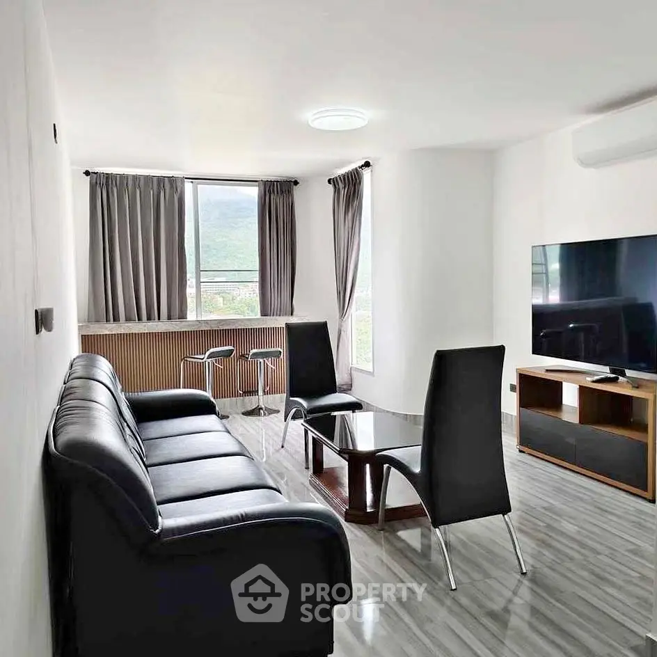 Modern living room with sleek black leather sofa, glass coffee table, and large TV, featuring mountain view.
