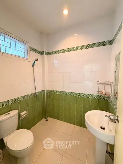 Charming bathroom with green and white tiles, featuring a shower, toilet, and pedestal sink.
