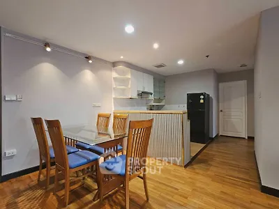 Spacious dining area with wooden flooring and modern kitchen in open layout apartment.