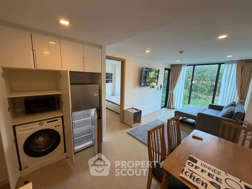 Modern open-plan living room with kitchen and dining area, featuring large windows and stylish furniture.